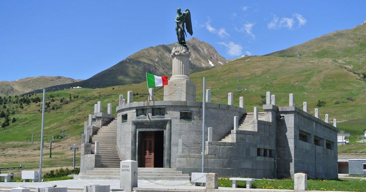 Un sacrario di montagna con bandiera italiana davanti alle cime
